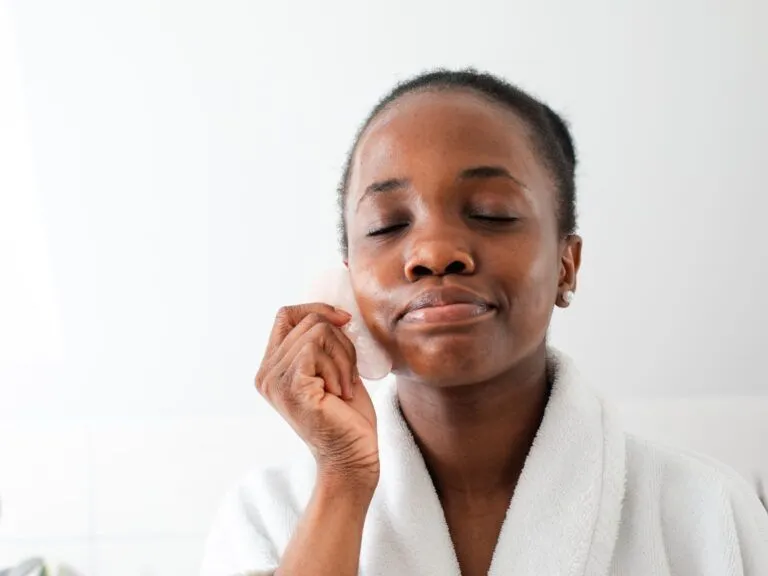 black woman doing facial gua sha massage with pink stone