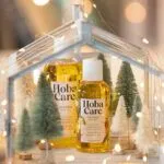 bottles of HobaCare golden jojoba surrounded by white fairy lights and white and green bottlebrush trees