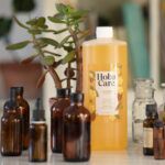 32 oz bottle of HobaCare golden jojoba oil surrounded by amber glass bottles of essential oils in various sizes