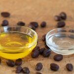 two small glass bowls on filled with golden unrefined jojoba oil and the other with clear deodorized jojoba there are jojoba seeds on the wooden tabletop around them