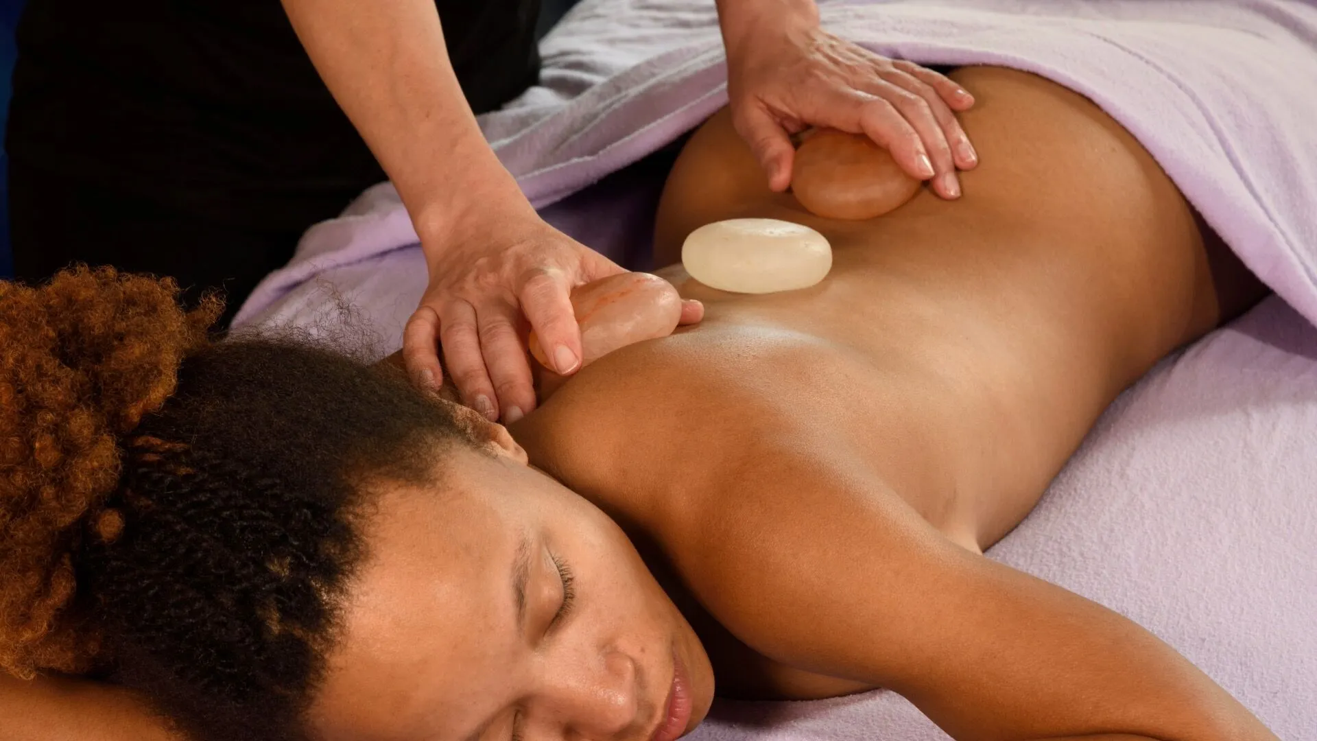 using jojoba oil and salt stones for massage on a dark skinned client