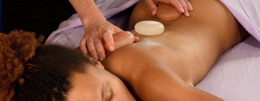 using jojoba oil and salt stones for massage on a dark skinned client