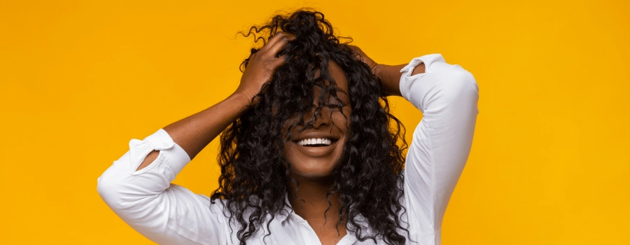 woman in white shirt with hands in textured hair standing in front of a bright yellow background