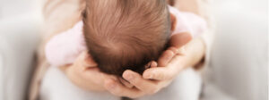 baby's small head with dark hair nestled in mom's hands