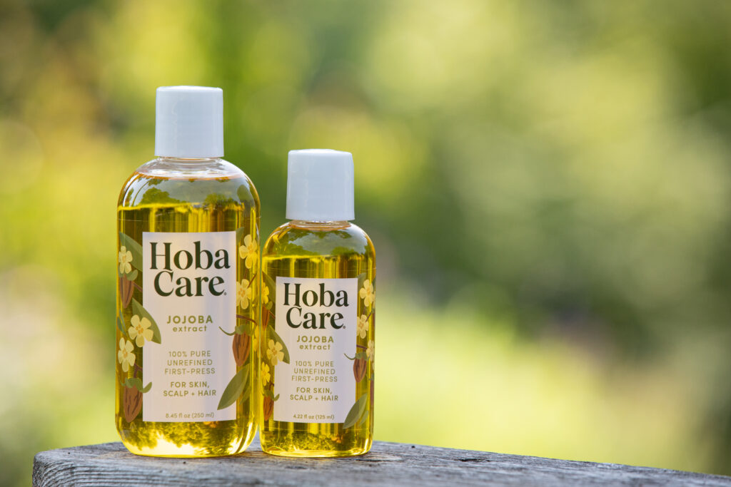 Golden HobaCare Jojoba a natural after skin sun soother in two clear bottles with a blurred green background