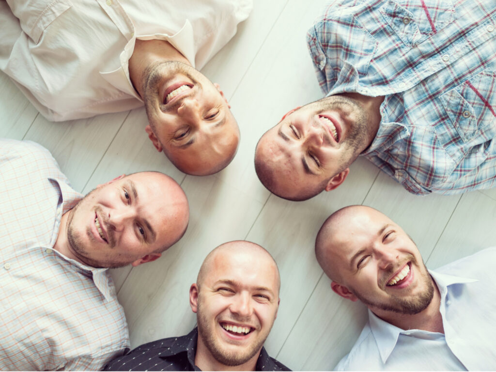 five bald headed men laying on a light wooden floor in diffused light to promote jojoba is best for bald heads
