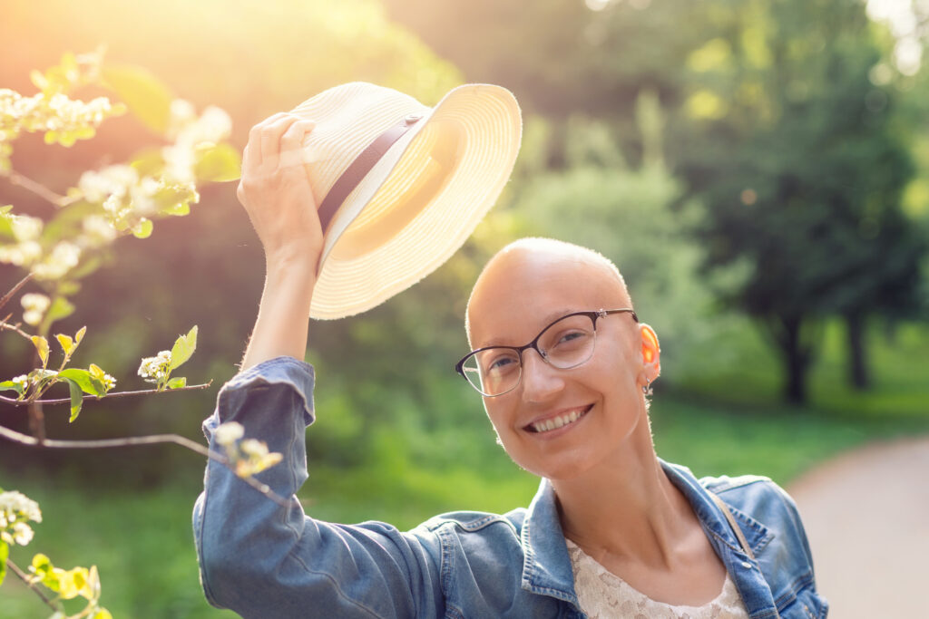 woman with bald head outdoors in the golden sunlight removing hat