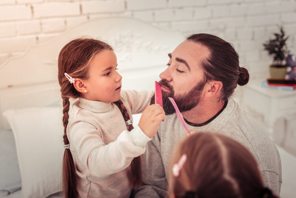 little girl with brown braids coming dad's brown beard with a pink comb
