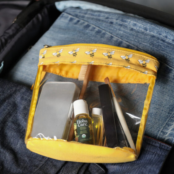 clear bag of toiletries containing travel size HobaCare Jojoba in suitcase