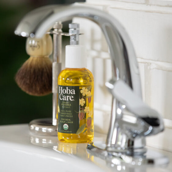 bottle of golden organic HobaCare jojoba on bathroom sink with old fashioned shaving kit in the background