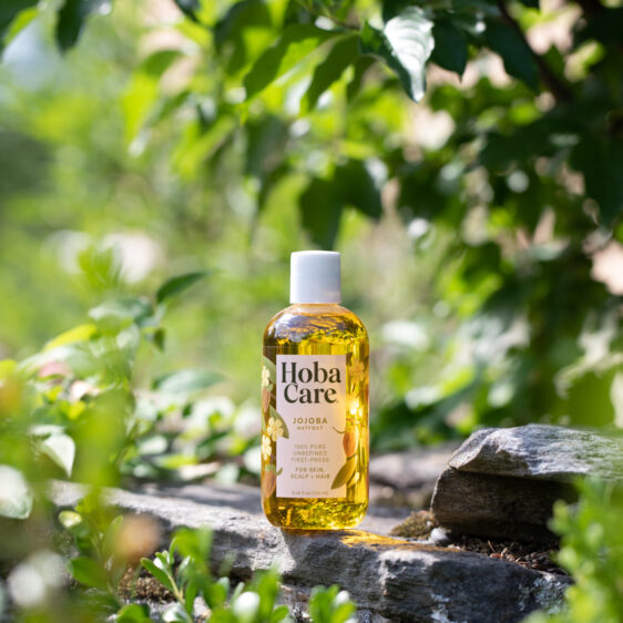 bottle of HobaCare golden jojoba outdoors in the sunshine on a rock surrounded by greenery