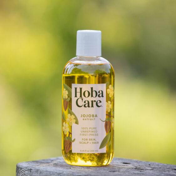 8.44 fl oz bottle of Golden HobaCare Jojoba outdoors with a blurry green background