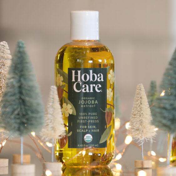 bottled of golden organic hobacare jojoba surrounded by green and cream bottlebrush trees and fairy lights
