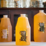bottles of golden HobaCare Jojoba in professional sizes in front of a dark wooden cabinet