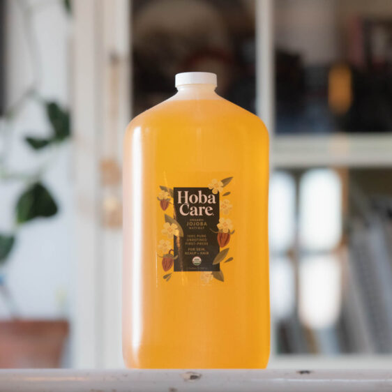 one gallon of HobaCare organic golden jojoba on a white surface with blurry office in background