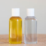 two clear bottles one filled with golden unrefined jojoba and the other will clear deodorized jojoba sitting on a wooden tabletop