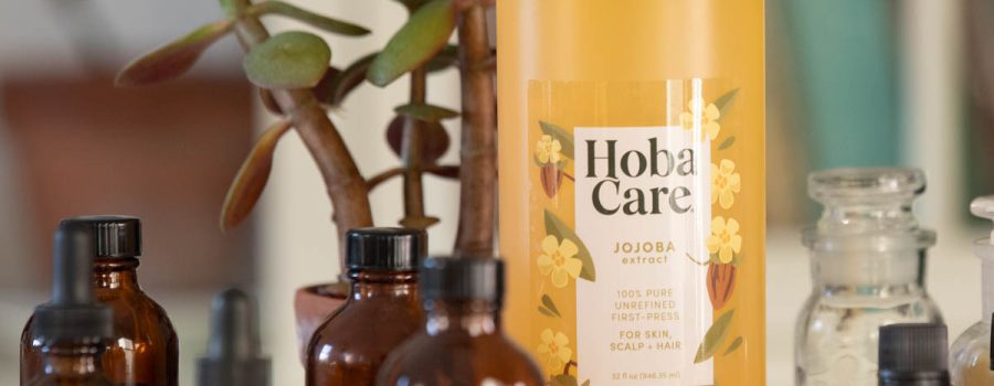32 oz bottle of HobaCare golden jojoba oil surrounded by amber glass bottles of essential oils in various sizes