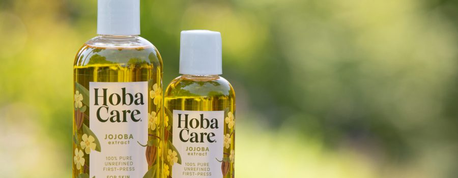 Golden HobaCare Jojoba a natural after skin sun soother in two clear bottles with a blurred green background