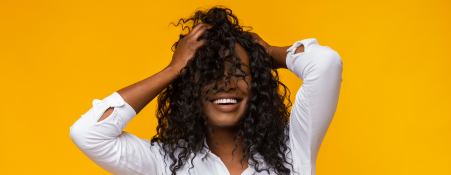 woman in white shirt with hands in textured hair standing in front of a bright yellow background