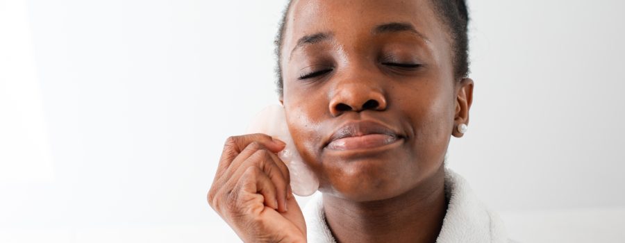 black woman doing facial gua sha massage with pink stone