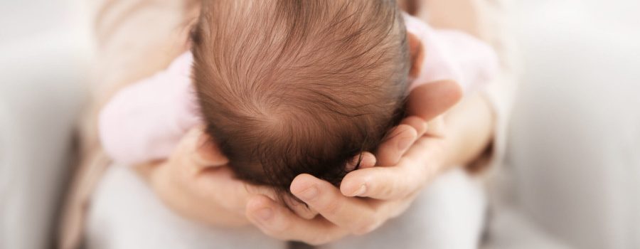 baby's small head with dark hair nestled in mom's hands